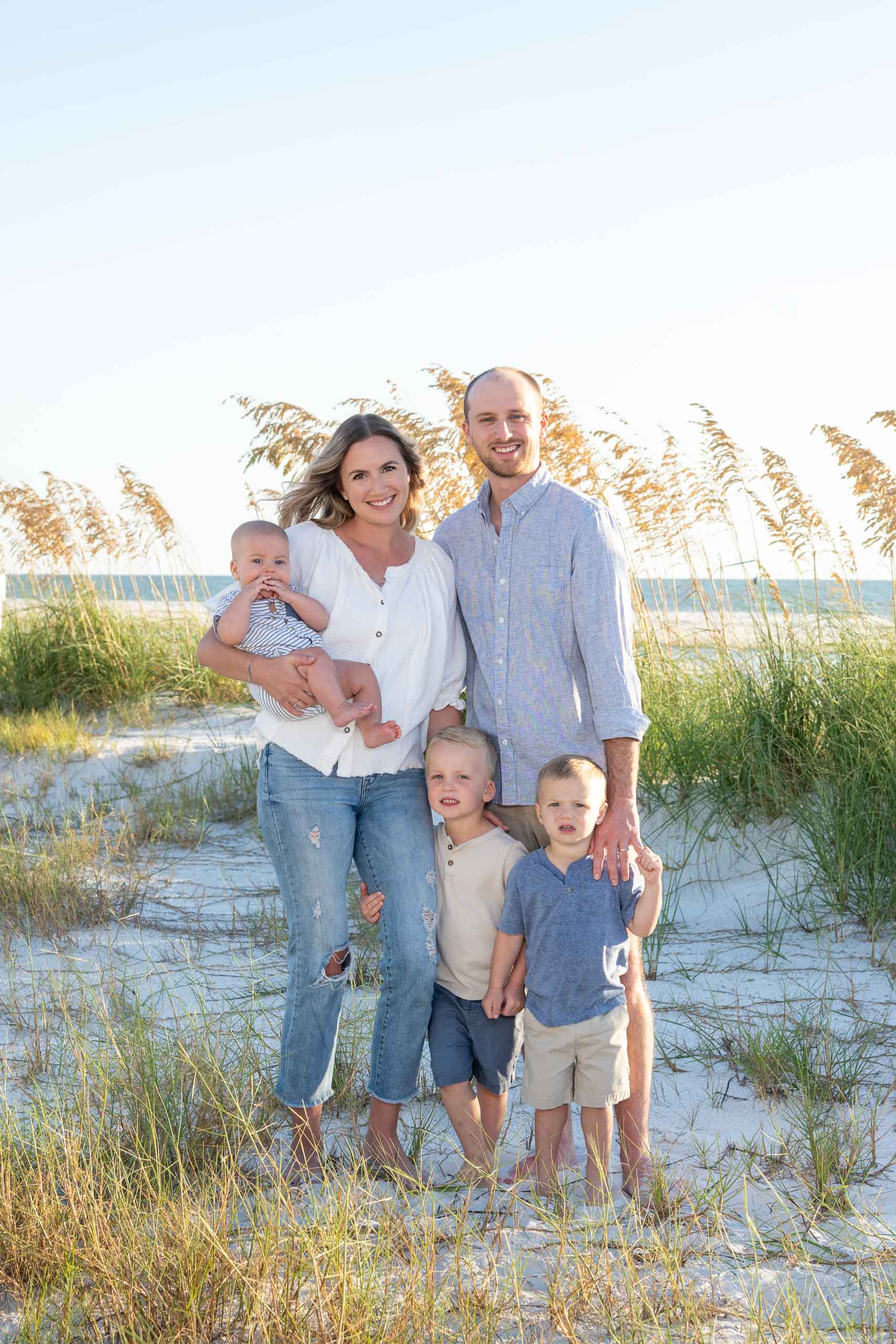 parents with their three children on the beach with sea grass behing them