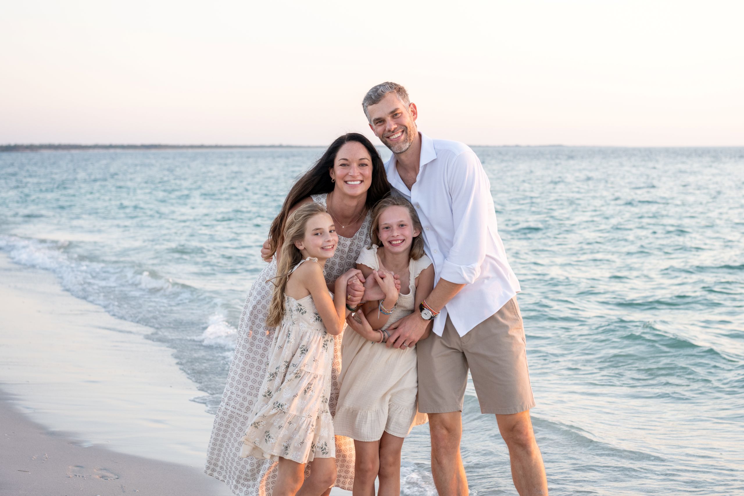 mom and dad wrap their arms around their daughters as they smile