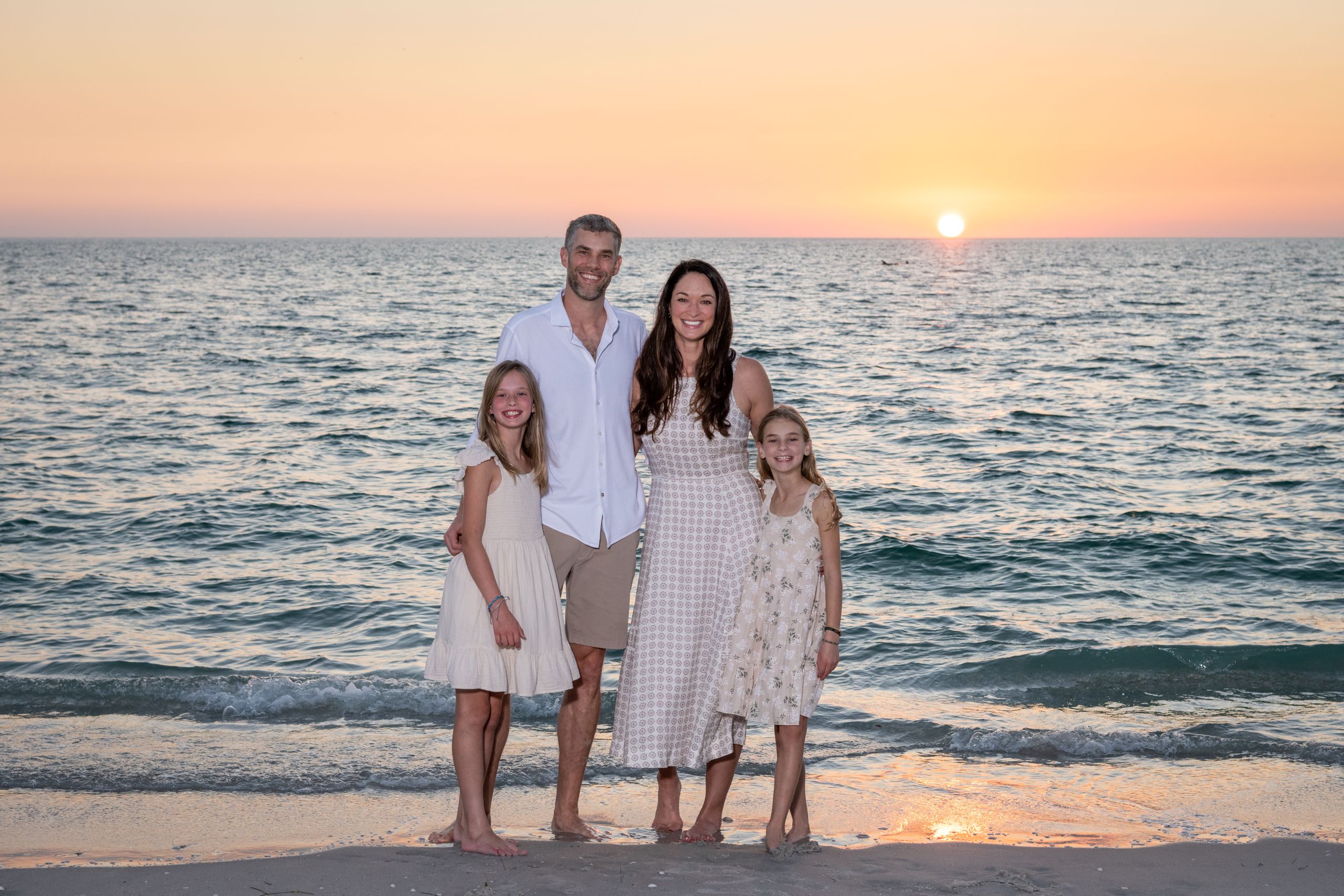 parents with their daughters at the beach with the sunset behind them