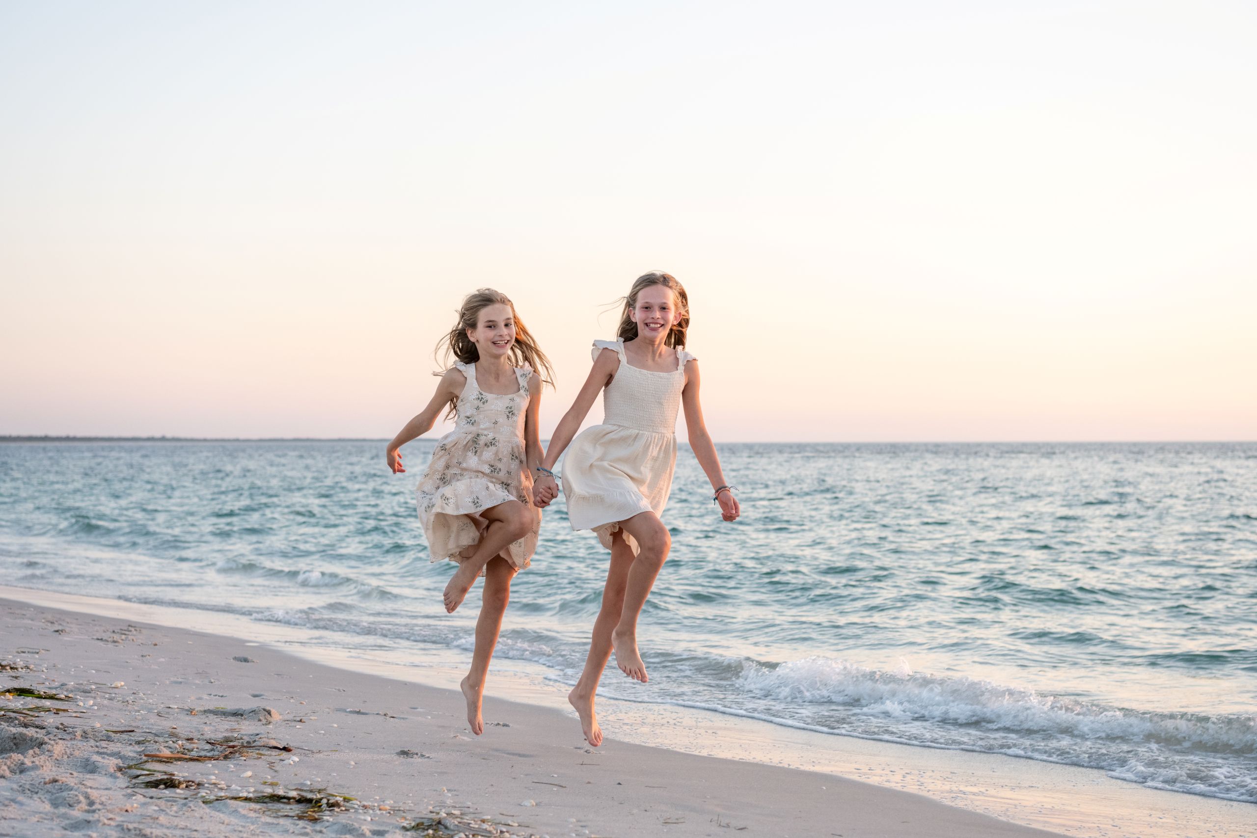 sisters hold hands and skip along the beach