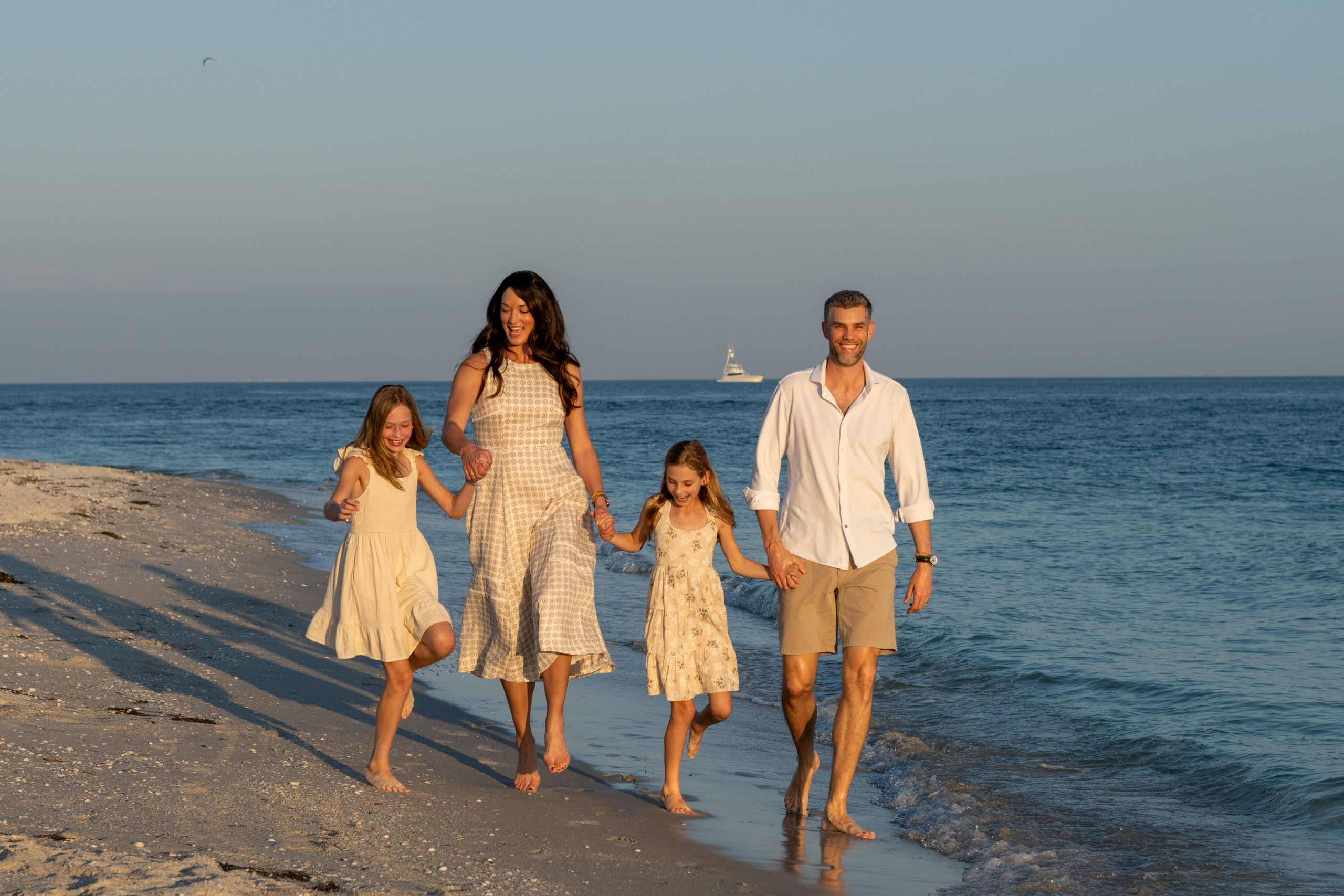 parents hold hands with their daughters as they walk and laugh as they walk along the shoreline