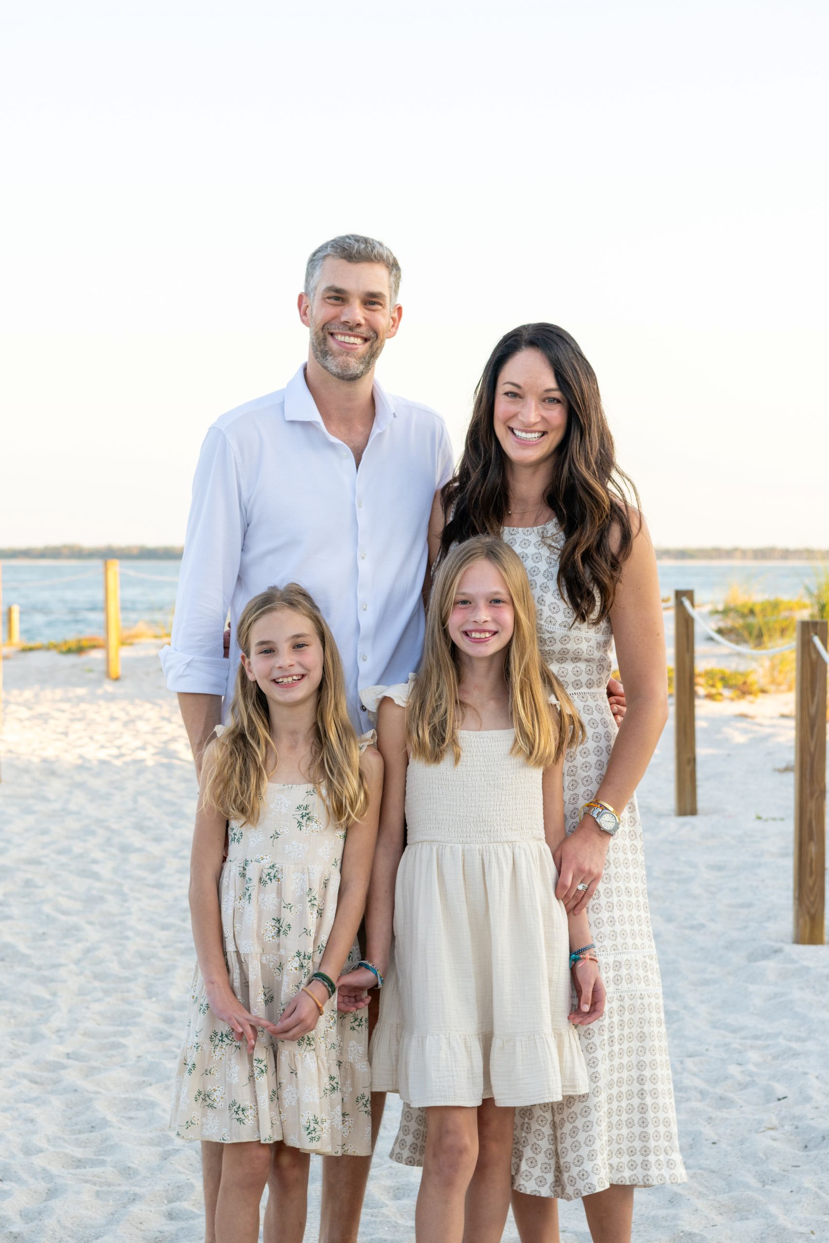 parents with their girls smiling while on the beach with the water behind them