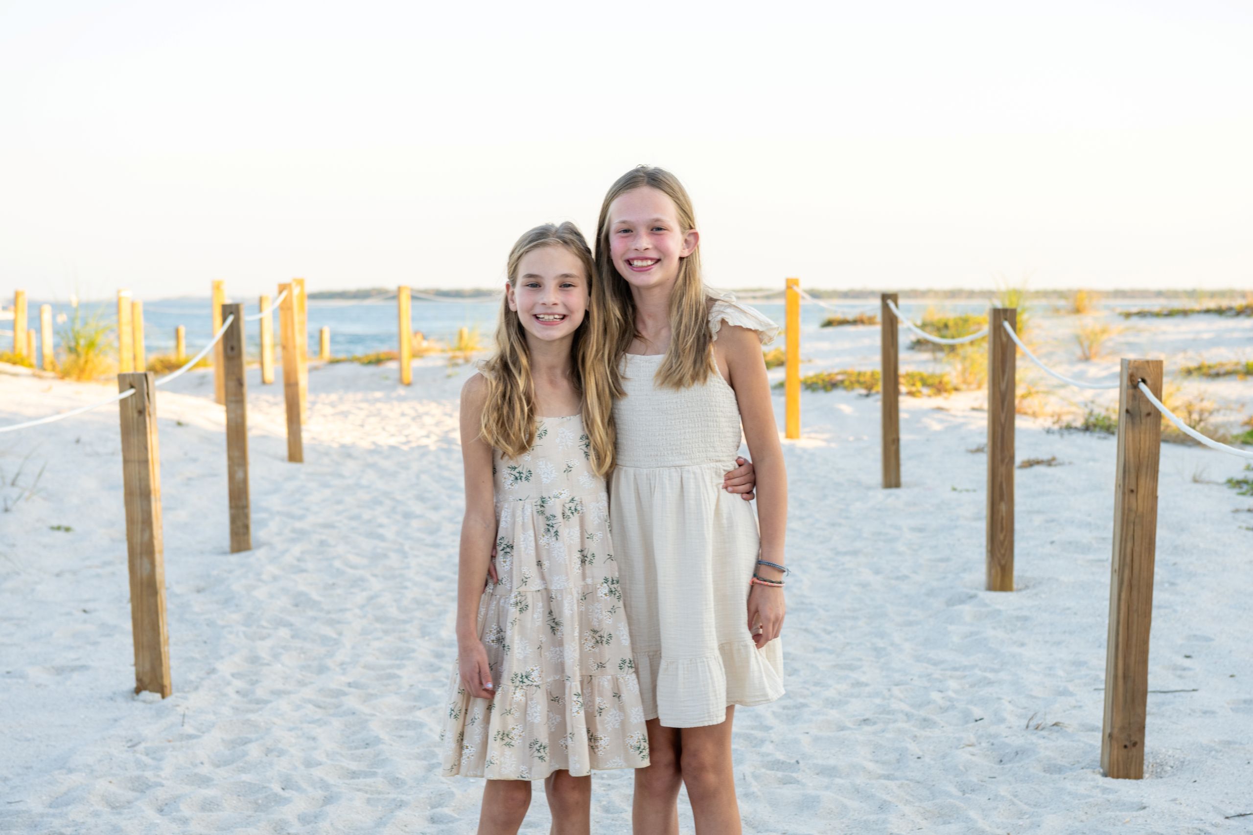 sisters smile as they stand close on the beach