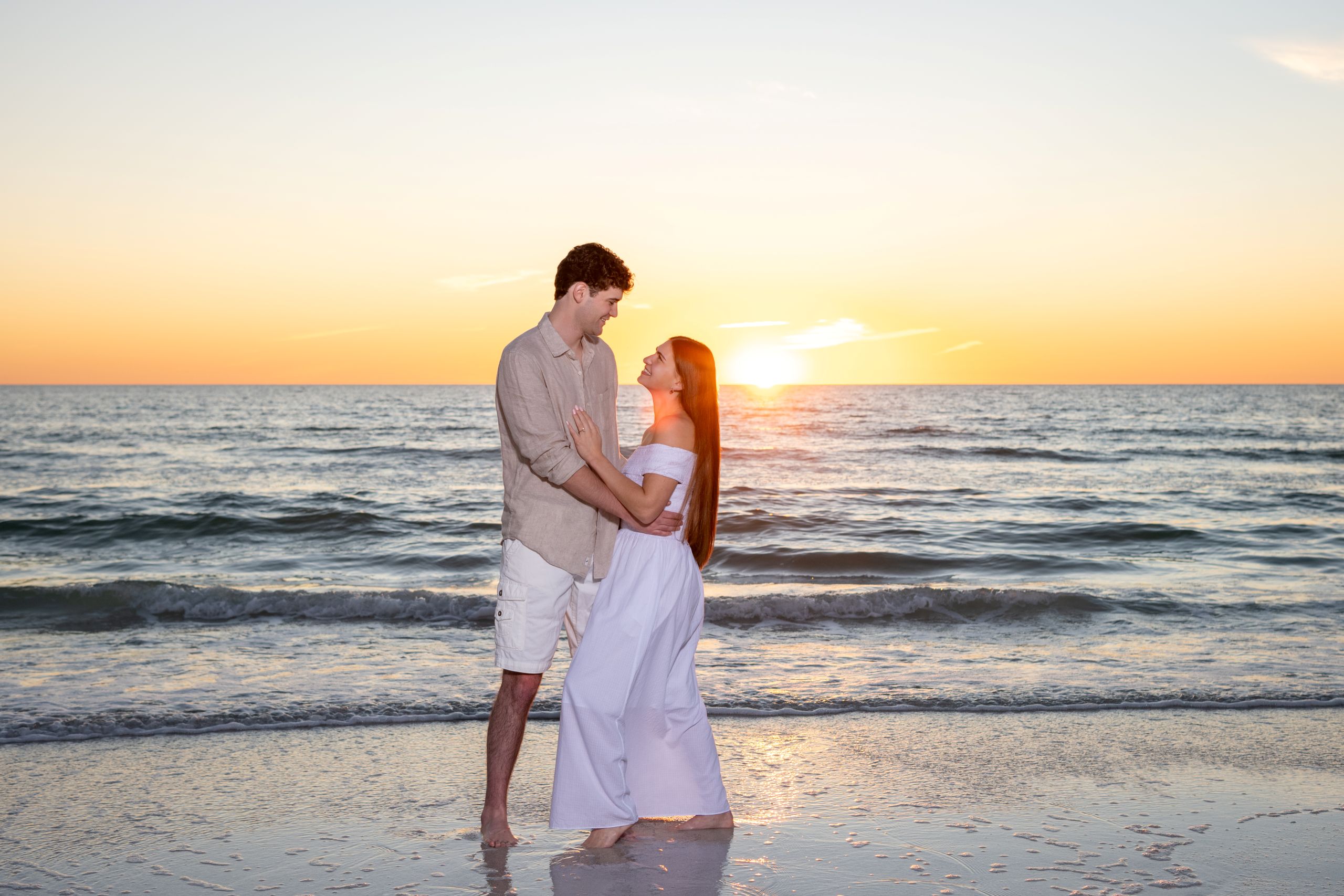 couple look lovingly at each other as they stand on the beach at sunset