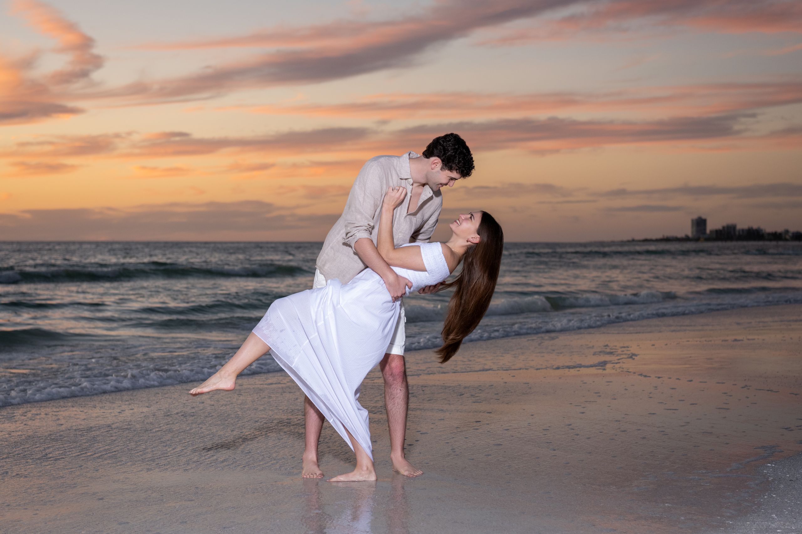 guy dips his fiance on the beach at sunset