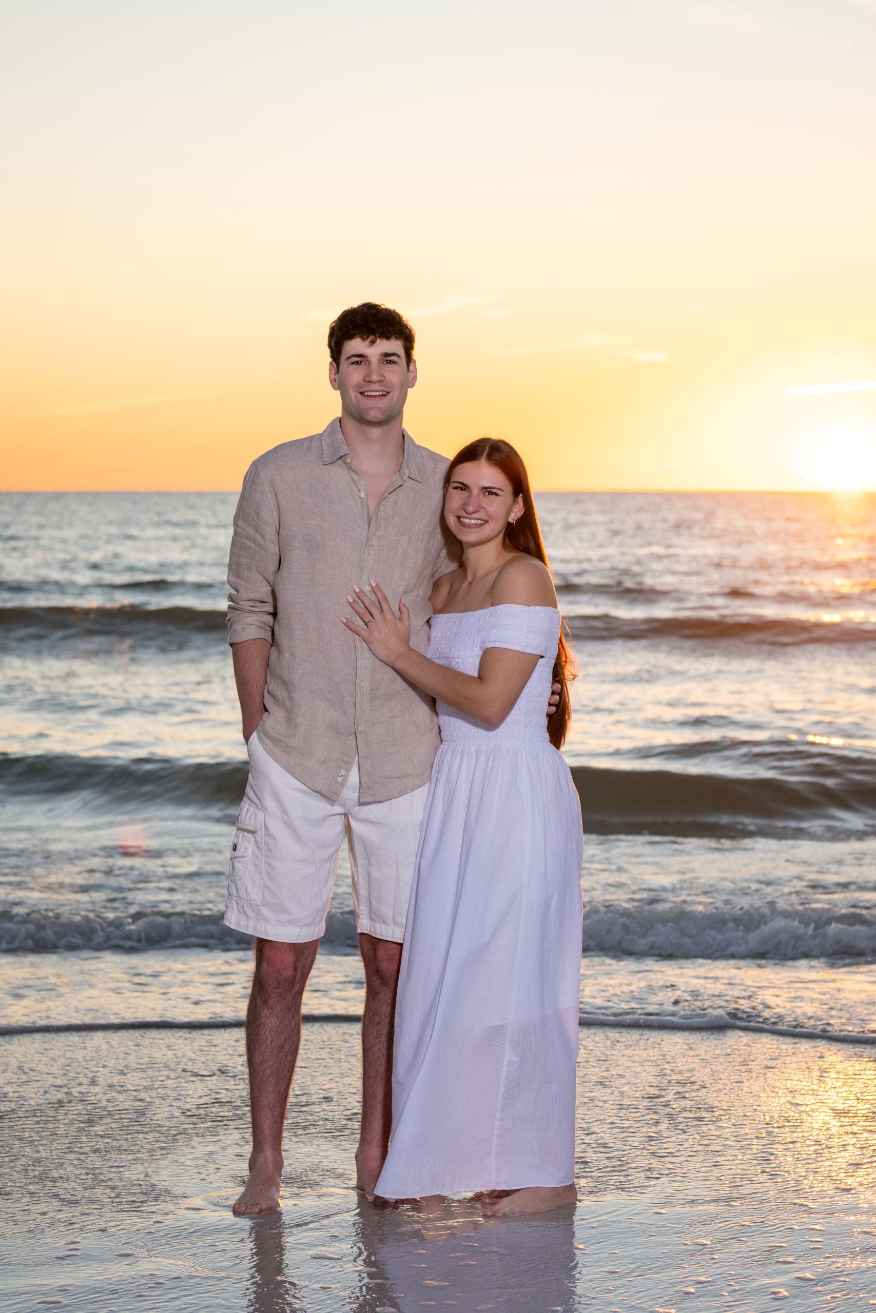 engaged couple smile as the sun sets behind them