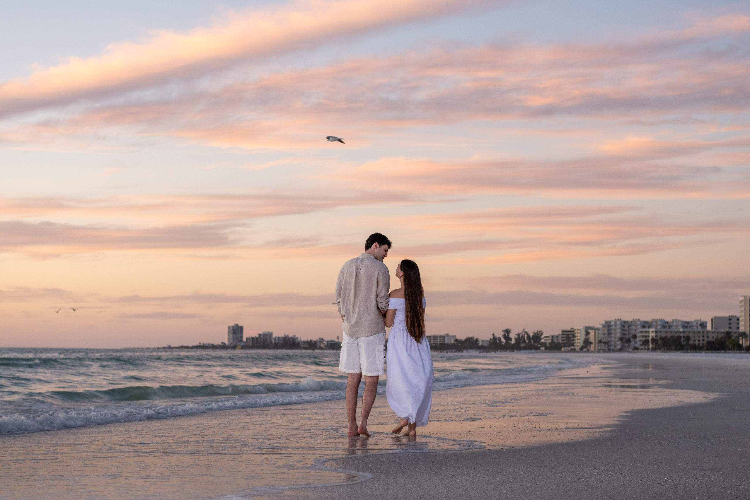 couple walking along Siesta Key as the sky turns pink after sunset