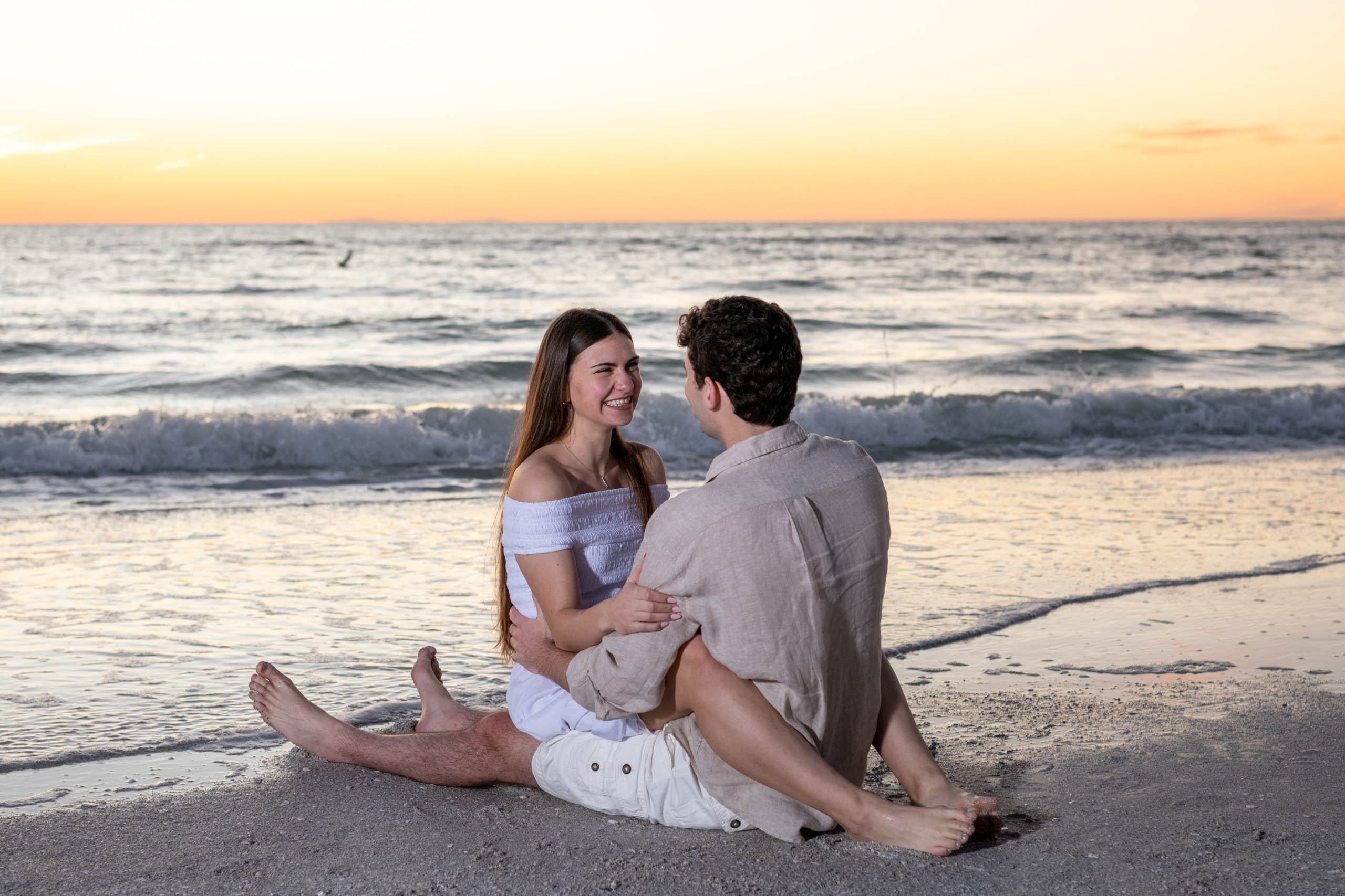 girlfriend sits on her fiances lap on the beach