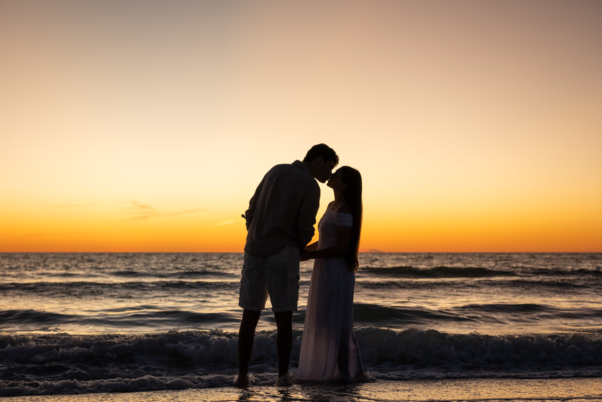 silhouette of couple kissing as they stand in the water after sunset