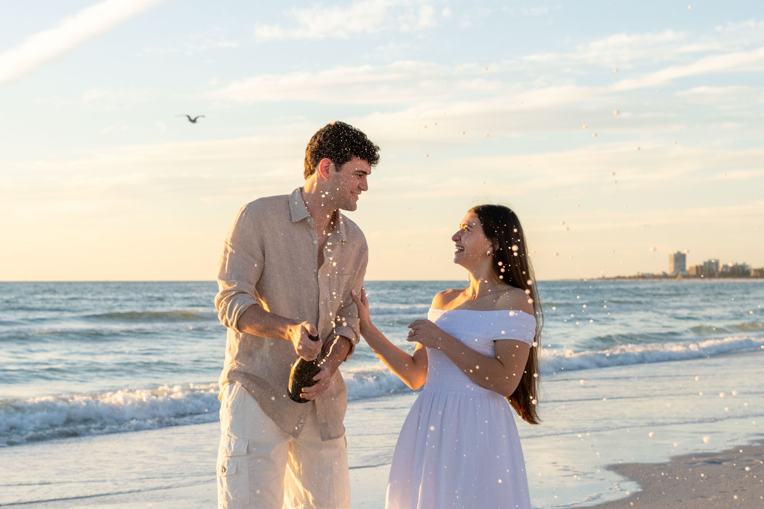 engaged couple smile at each other as they spray champagne