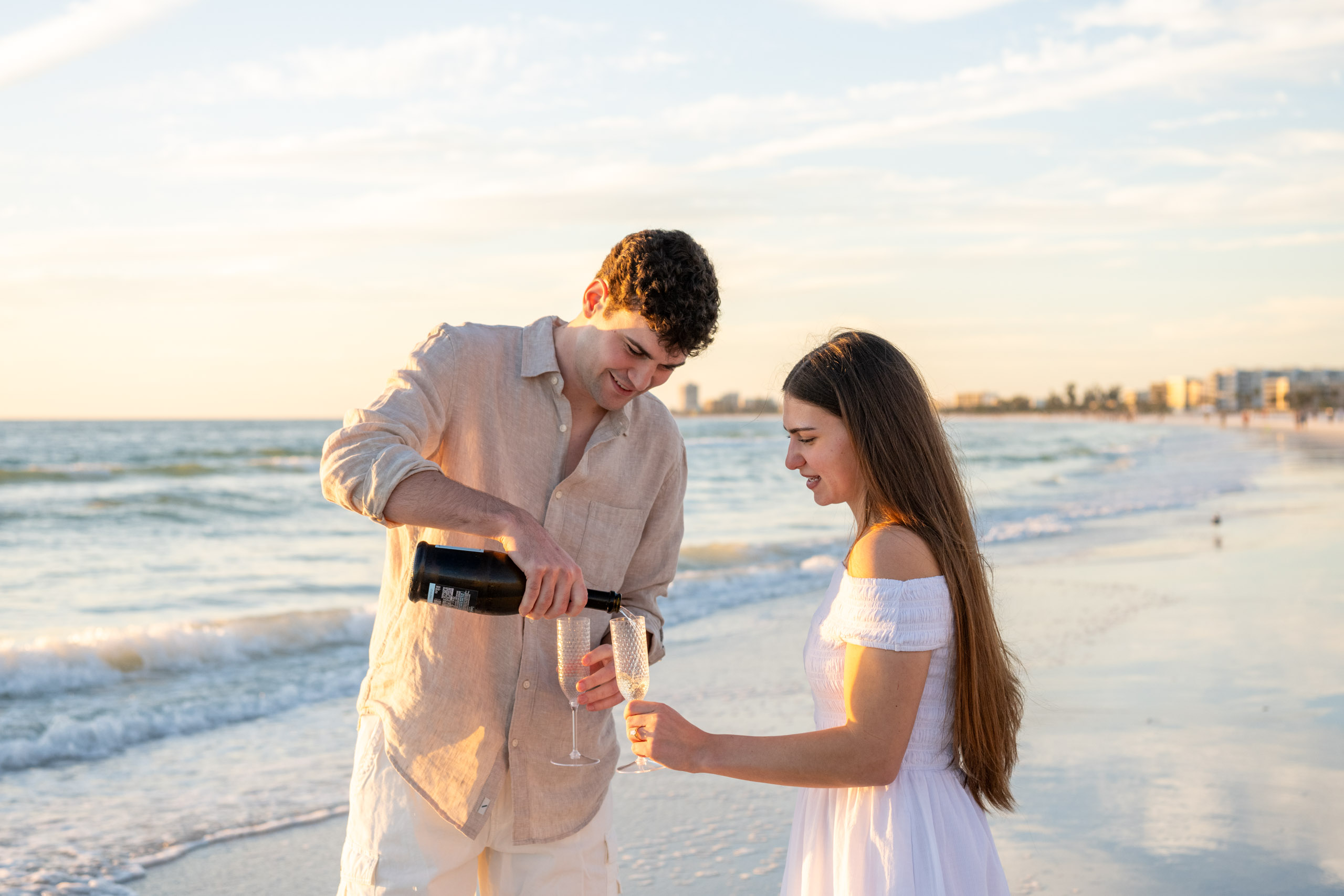 guy pours champagne into their glasses as his fiance looks on