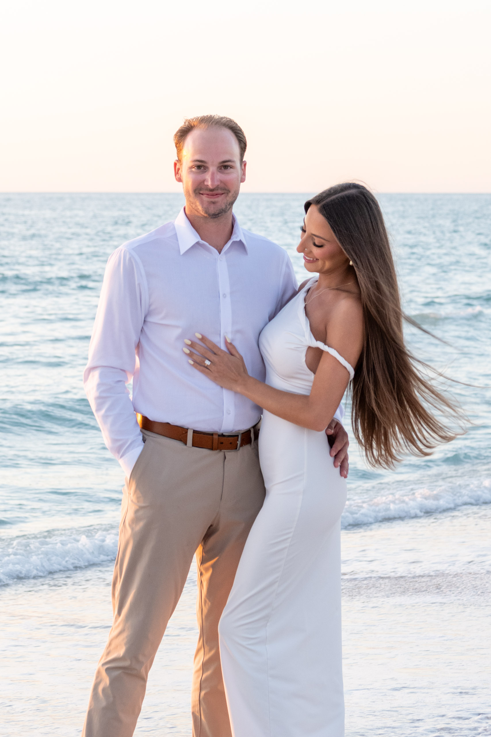 couple holding each other close and woman looks down at her engagement ring