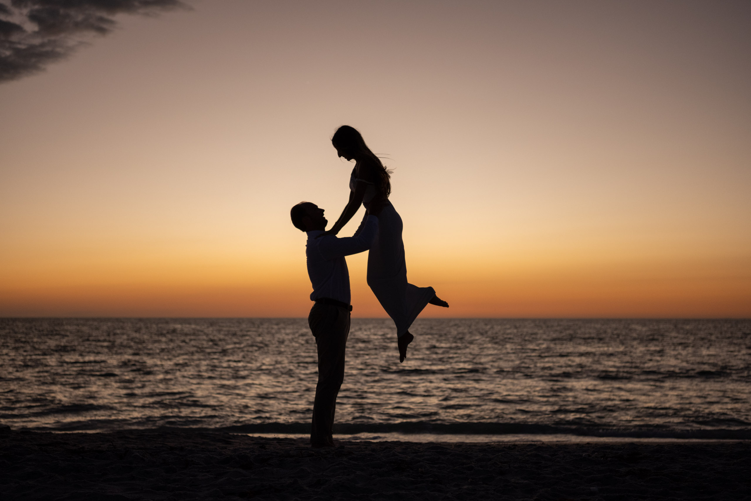 silhouette of guy lifting up his fiance on the beach after sunset