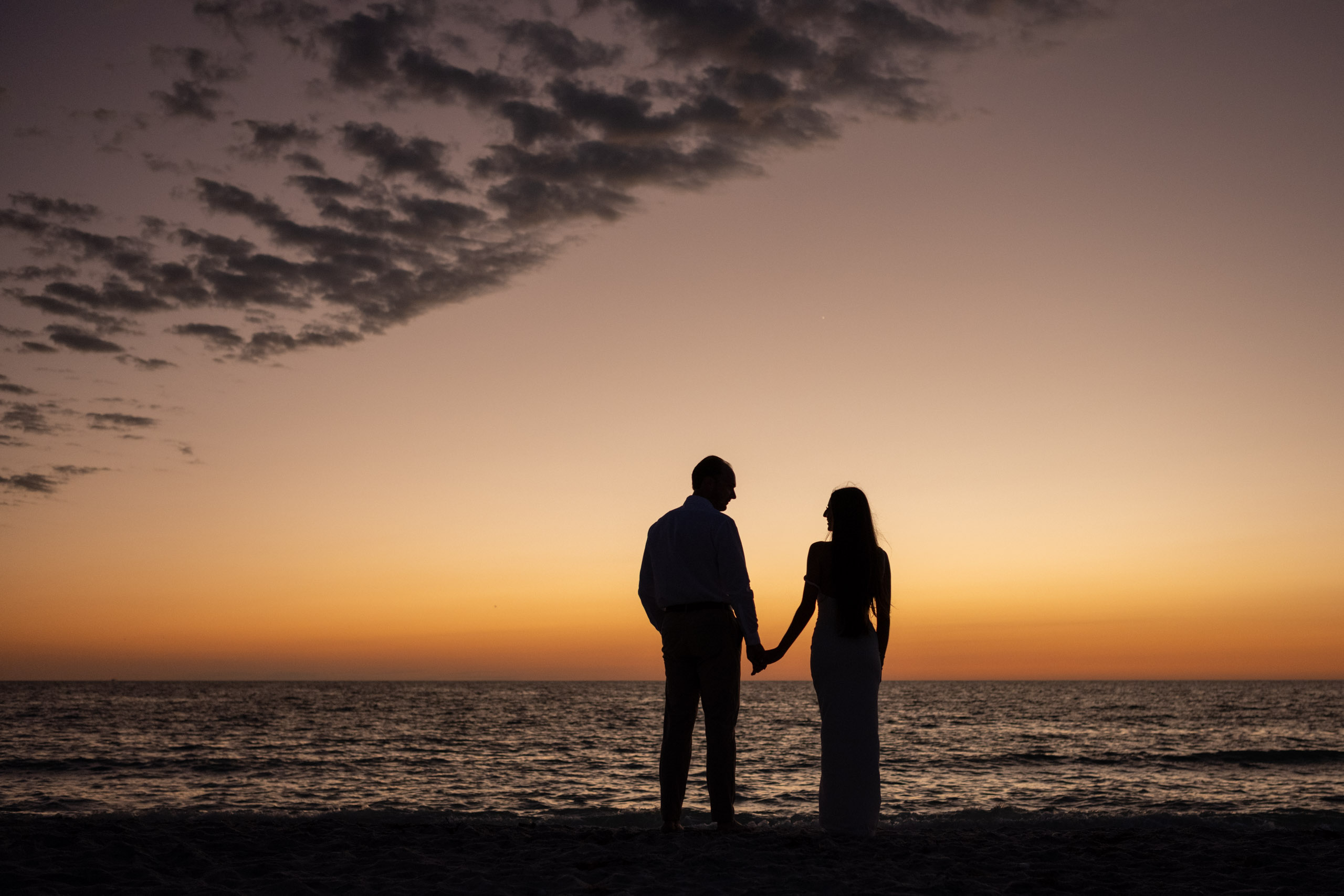 silhouette of couple holding hands on the beach after sunset