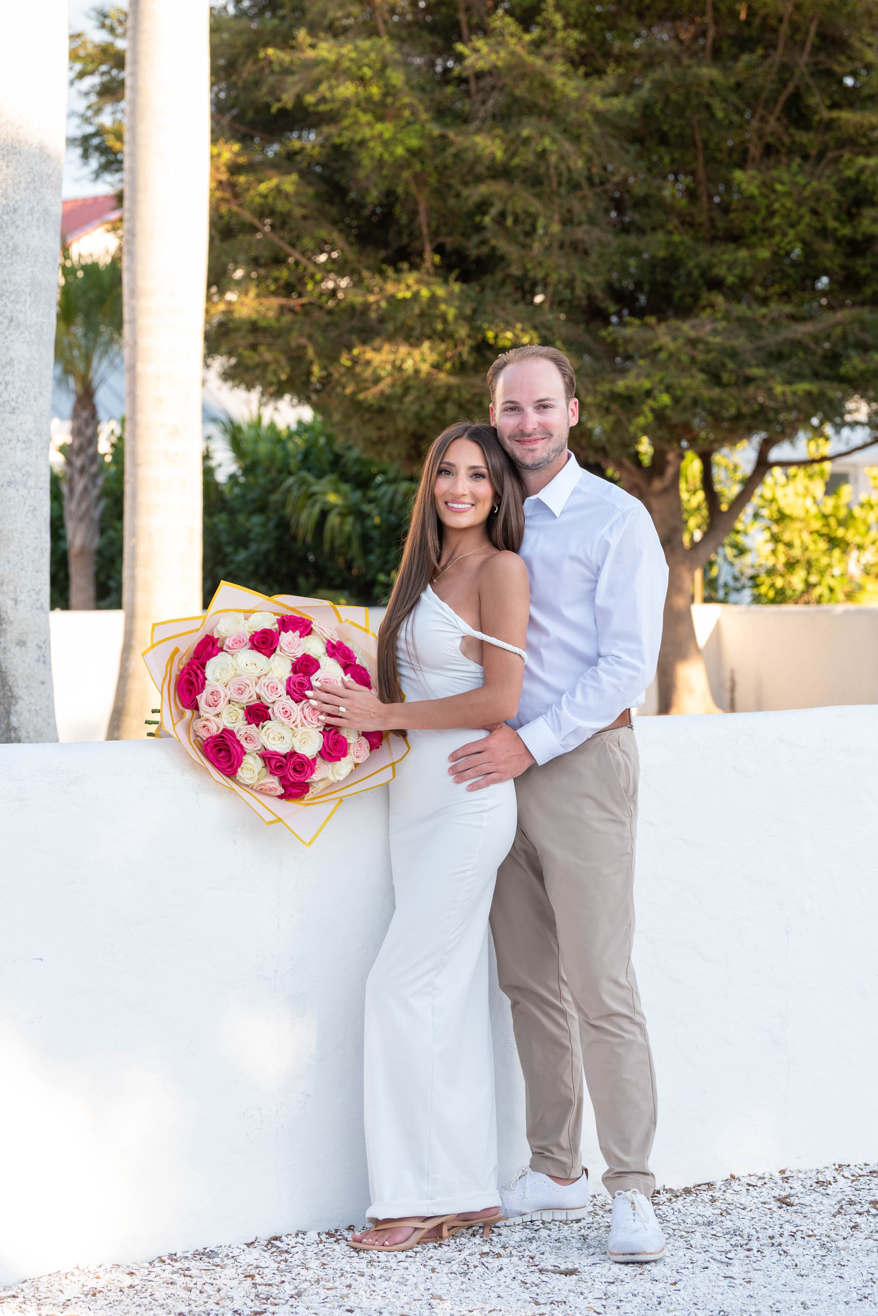 couple show off a bouquet of three dozen roses and her engagement ring.