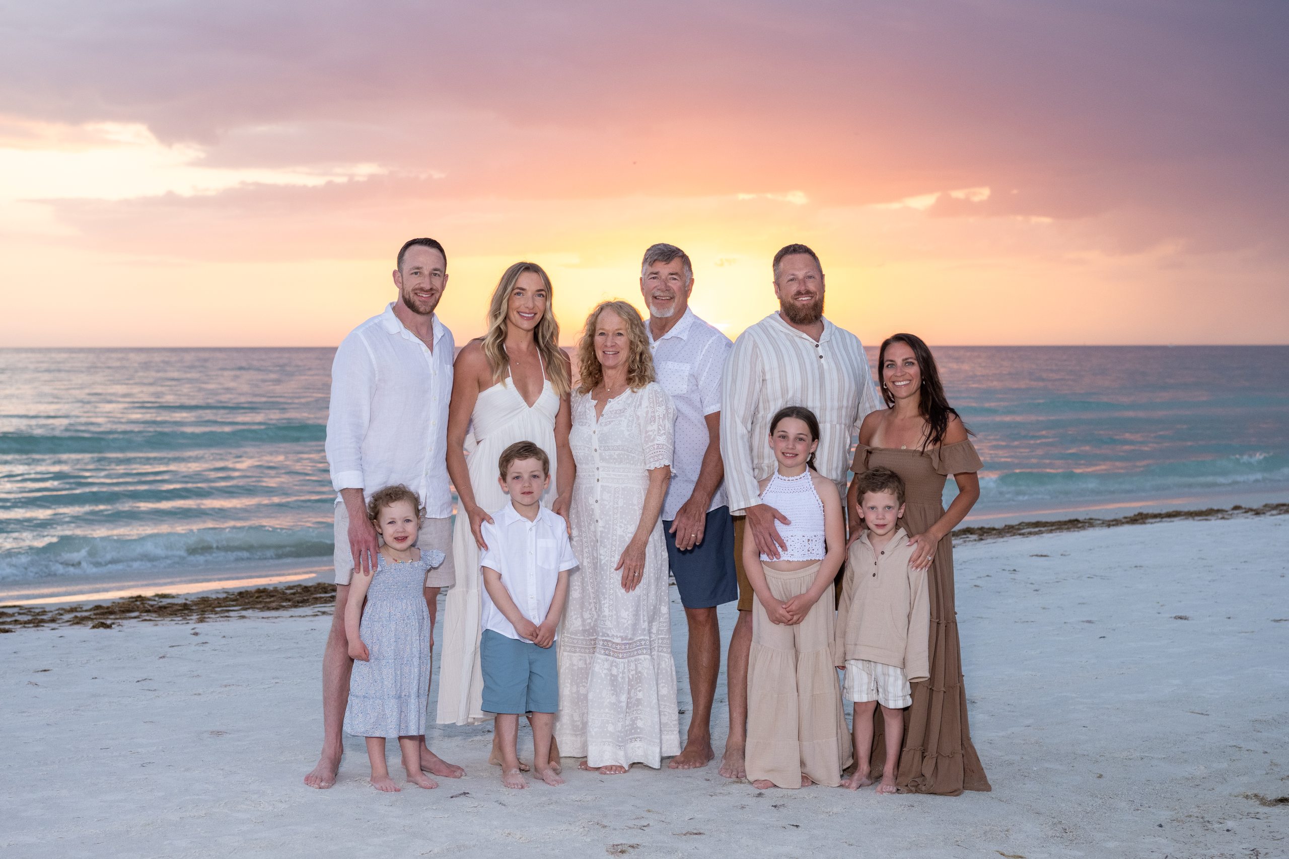 family stands together posing on the beach at sunset
