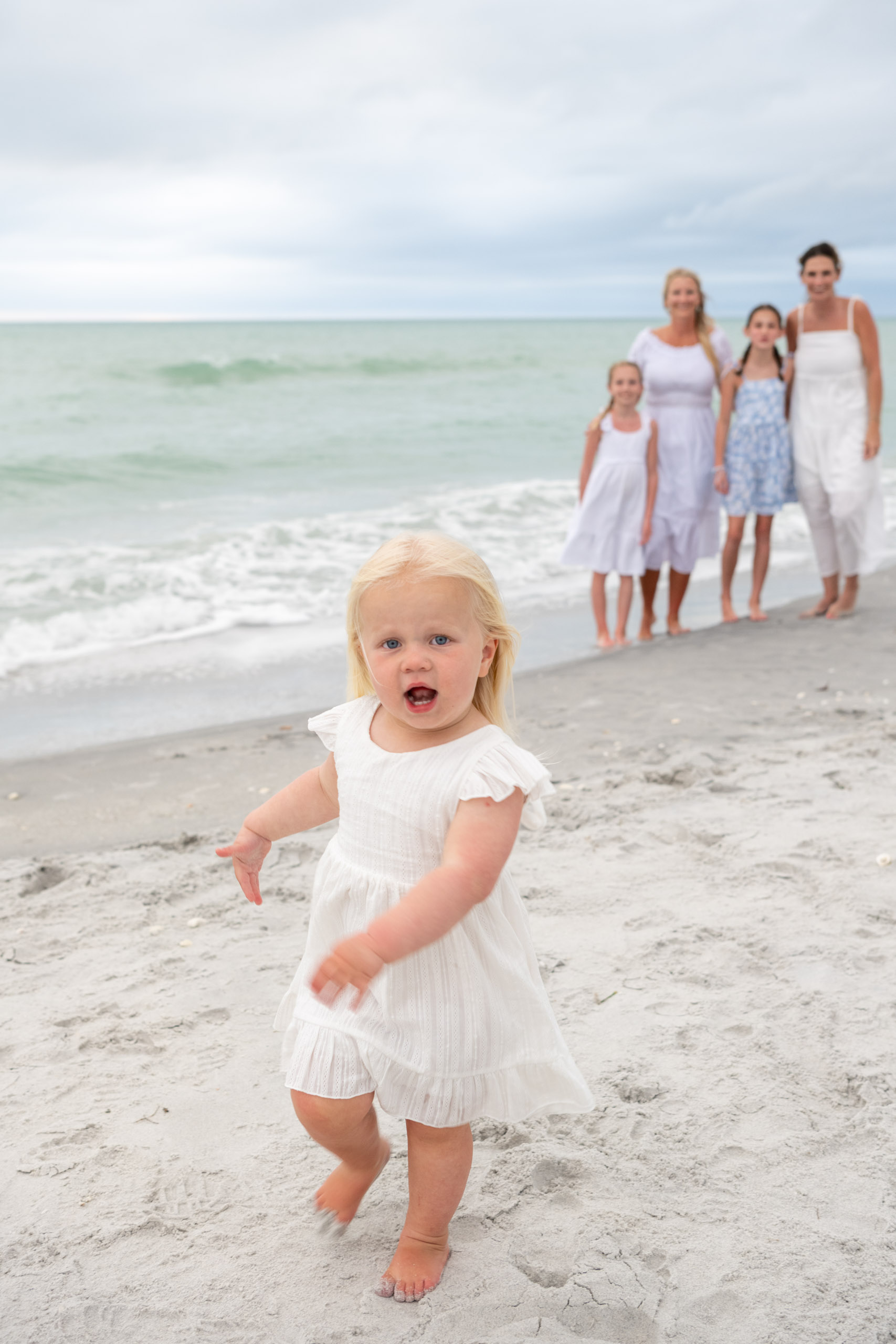 little girl runs towards the camera with her family laughing in the background