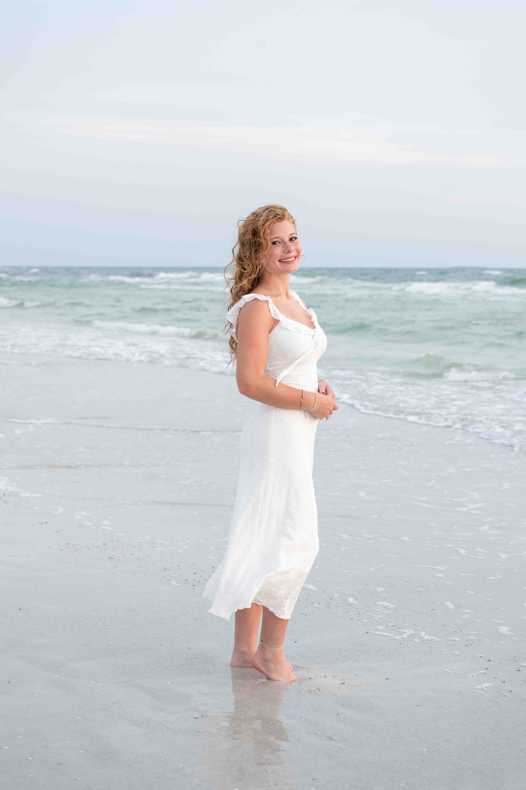 senior girl standing on beach in a long white dress and smiling