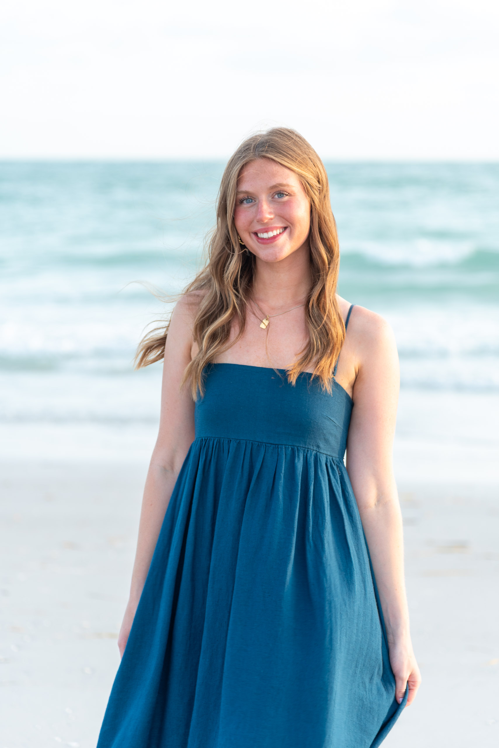 senior girl with long hair and teal dress standing by the Gulf